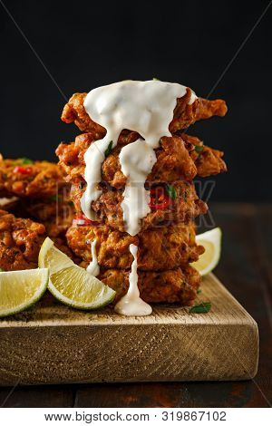 Indian Takeaway Food, Spicy Onion Bhajis Served With Chili Yoghurt Dip And Lime Wedges On Wooden Boa
