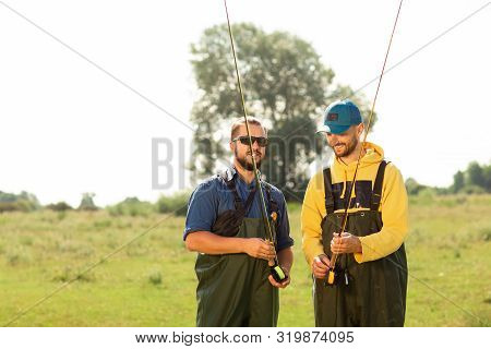 Two Fishermen Preparing For Fishing. They Hold The Fishing Rods And Talk To Each Other. Sport Fishin