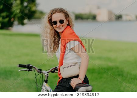 Happy Curly Haired Blonde Woman Enjoys Bicycle Ride, Has Her Own Transport, Leads Healthy Lifestyle,