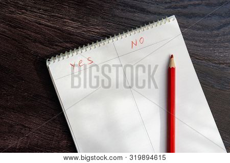 A Notebook With The Words Yes And No And A Red Pencil Lie On A Wooden Surface. The Concept Of Analys