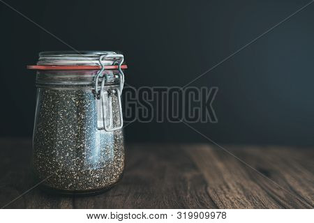 Close-up Shot Of Chia Seeds In Glass Weck Jar On Wooden Table Against Dark Background