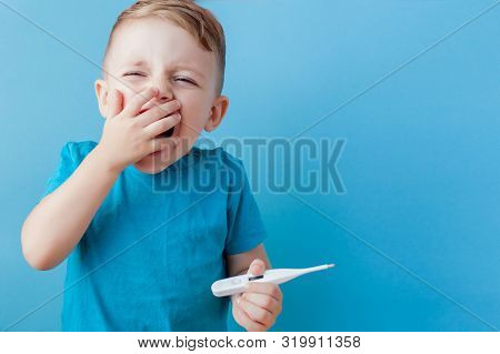 Ill Young Child With A Thermomether, Measuring The Height Of His Fever And Looking Into The Camera