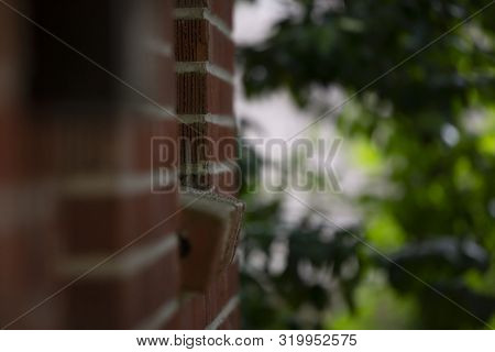 Red Brick Wall And Window Sill Against A Dreary Grey Background With Vibrant Green Bushes