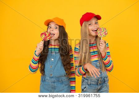 Having A Lick. Little Girls Enjoying Delicious Taste Of Lollipops On Yellow Background. Small Childr