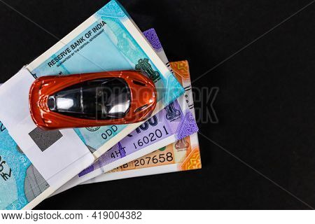 An Orange Red Toy Car Placed On Bundles Of Money Shot Over Black Surface With Copy Space