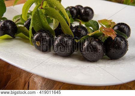 Jabuticaba, Jabuticabas In Detail Inside A White Plate With Branches And Leaves On Rustic Wood, Sele