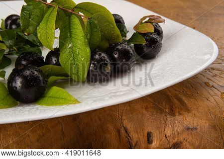 Jabuticaba, Jabuticabas In Detail Inside A White Plate With Branches And Leaves On Rustic Wood, Sele