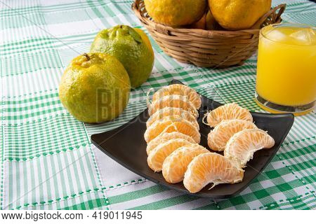 Orange Ponkan, Orange Ponkan Slices On A Black Plate, Plus Some Oranges And A Glass Of Juice On A Ch