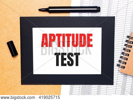 On A Wooden Table, There Is A Black Open Marker, A Brown Notepad And A Sheet Of Paper In A Black Fra