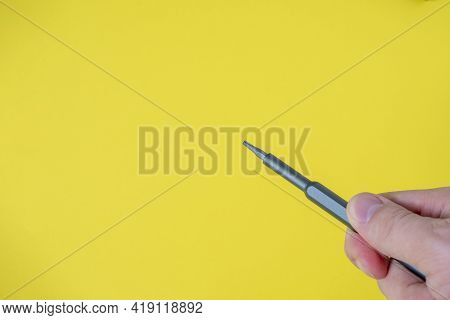 A Man's Hand Holds A Small Screwdriver With A Torx Nozzle On A Bright Yellow Background. Copy Space,