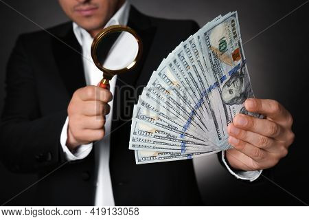 Expert Authenticating 100 Dollar Banknotes With Magnifying Glass Against Dark Background, Closeup. F
