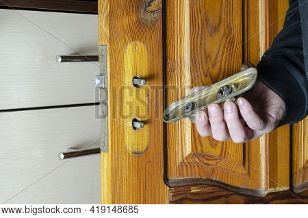 A Man Removes An Old Mortise Lock On A Wooden Interior Door. The Hand Holds The Overlay Bar Of The L