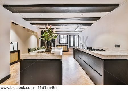 Design Of Open Plan Kitchen With Stone Counters And Island In Middle Under Ceiling With Wooden Beams