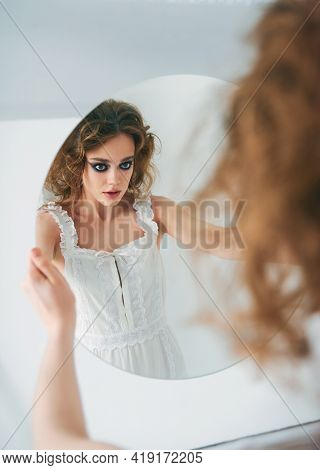 Portrait Of Pretty Strange Freaky Girl. Beautiful Odd Woman In White Dress Looking Into The Mirror