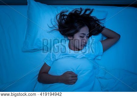 Top View Of Beautiful Young Woman Sleeping Cozily On A Bed In His Bedroom At Night. Blue Nightly Col