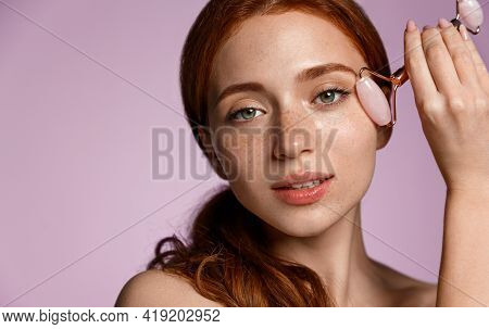 Skincare Spa. Close Up Redhead Woman Uses Natural Quarz Roller Under Eye, Reduce Puffiness And Dark 