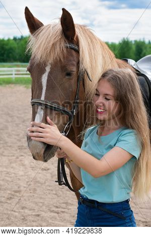 Portrait Of Smiling Young Woman With Blond Long Hair Is Caressing Brown Horse Snoot With Big Nostril