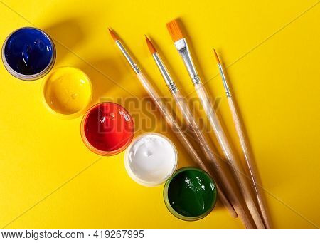 Paintbrushes And Colored Gouache Stands On A Yellow Background
