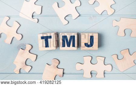 Blank Puzzles And Wooden Cubes With The Text Tmj Lie On A Light Blue Background.