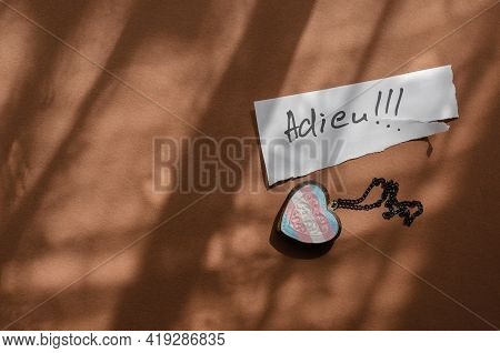Handwritten Word Adieu On A White Piece Of Paper And A Wooden Amulet In The Shape Of A Heart. Neck C