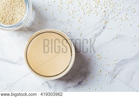 Sesame Paste - Tahini In A Glass Jar, White Marble Background. Israeli Cuisine Concept.