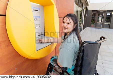 Happy Disabled Handicapped Woman In Wheelchair Using Atm Cash Macjine And Smiling At Camera On Sunny