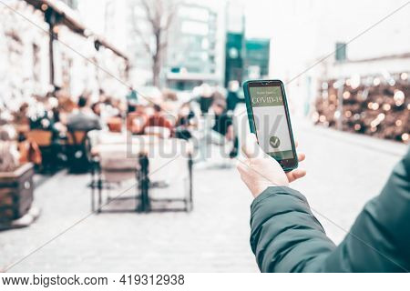 Vaccinated person using immunization certificate on smartphone at the restaurant or terrace. 