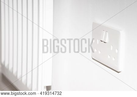 A United Kingdom Standard Wall Socket On A White Wall Next To Radiator