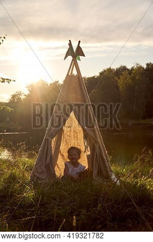 A Little Girl Is Sitting By The Lake. Sunny Akat. Wigwam. Happy Child.