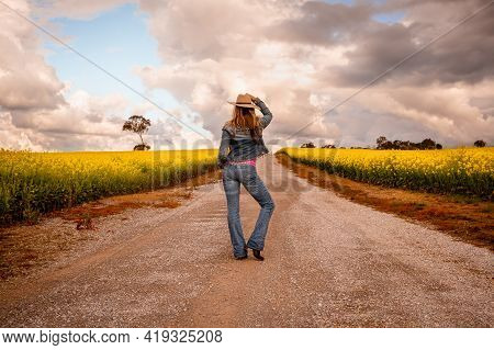 Aussie Country Girl Wearing Demin Jeans And Jacket Standing In Middle Of A Dirt Road In Farm Fields 