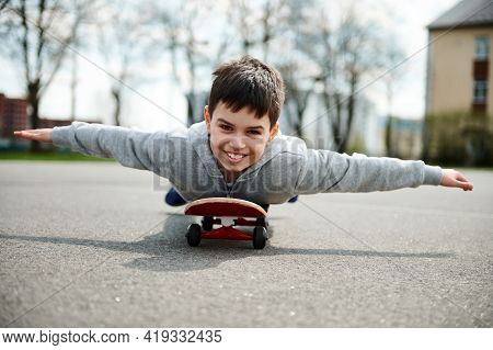 A Cute Boy Lying With His Belly On A Skateboard With His Arms Outstretched Like Wings And Imagining 