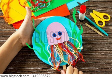The Child Is Holding Puppet Stics Toy Octopus On A Wooden Table. Handmade. Childrens Creativity Proj