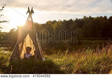 A Little Girl Is Sitting By The Lake. Sunny Akat. Wigwam. Happy Child.