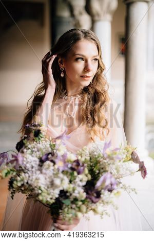Bride In A Beautiful Pink Dress Holds A Bouquet Of Wildflowers In Her Hand And Tucks A Lock Of Hair 