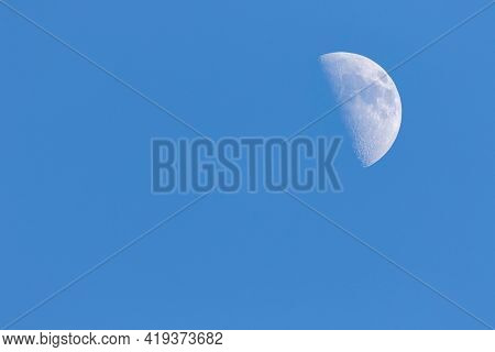 A Portrait Of A Half Moon During Day Time In A Blue Sky. The Craters On The Visible Have Of The Sate