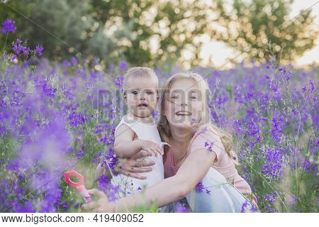 Two Blond Sisters In Flowers At Sunset