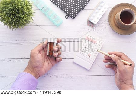 Person Hand Holding Pill Container And Calendar