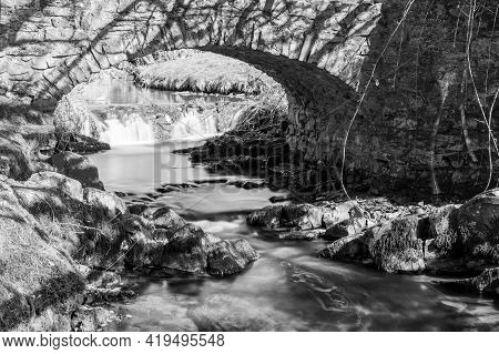 Long Exposure Of The Weir Water  River Flowing Under Robbers Bridge In Exmoor National Park