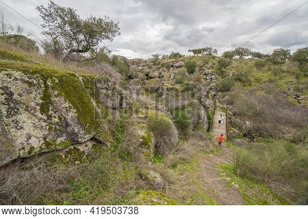 Children Crossing River Muelas Bridge Close To Granitic Caves. Cornalvo Natural Park, Extremadura, S