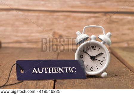 White Clock And Label Tag Written With Authentic On Wooden Board.