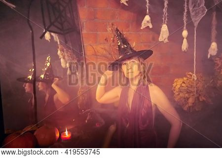 Blonde Witch In Red Dress And Black Hat With Candle And Mirror In Halloween Decoration Indoors.