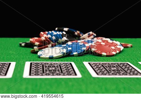Poker Chips On A Gaming Table In A Casino With Dramatic Lighting. Green Table And Black Night Backgr