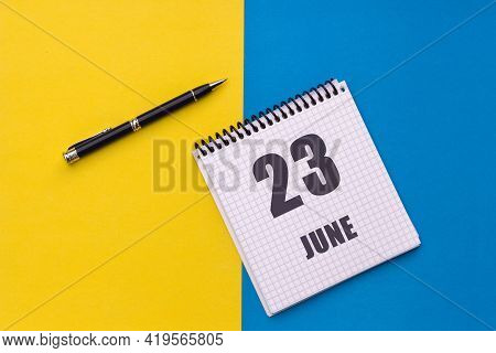 June 23th. Day 23 Of Month, Calendar Date. Notebook With A Spiral And Pen Lies On A Yellow-blue Back