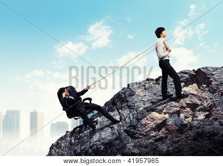 Imagem de dois jovens empresários, puxando a corda no topo da montanha contra o fundo da cidade