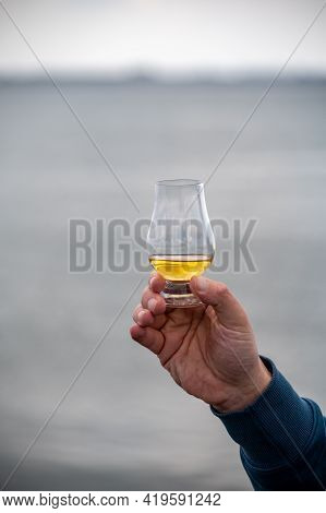 Hand With Dram Of Single Malt Scotch Whisky On Seashore In Scotland