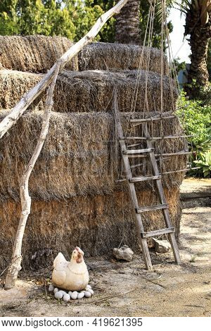 Straw Bales Stacked Next To Wooden Ladder And Figurine Of A Chicken