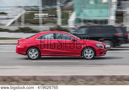 Side View Rolling Shot With Red Car In Motion. Mercedes Cla Class Driving Along The Street In City W