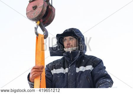 A Portrait Of A Fitter In A Blue Jacket At The Hook Of A Truck Crane