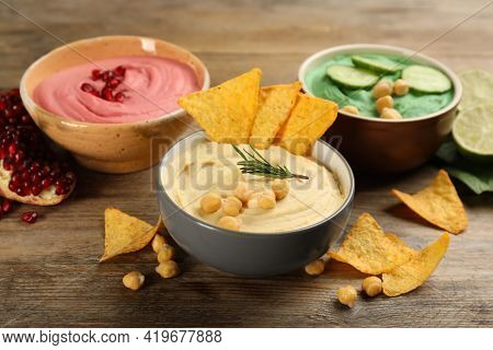 Different Kinds Of Tasty Hummus, Nachos And Ingredients On Wooden Table