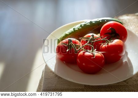 Tomatoes On A Branch And A Cucumber On A White Plate. Backlit Photo. Copspace